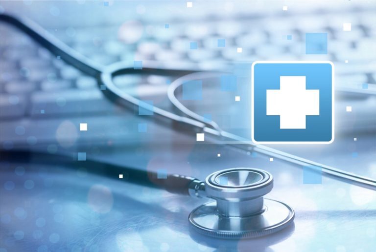 A stethoscope lying on a reflective surface in front of a computer keyboard, symbolizing digital healthcare or telemedicine, with a blue medical cross icon and abstract digital squares overlaying the image.