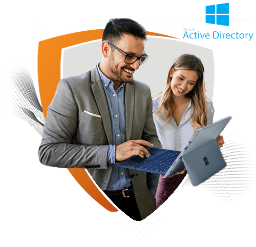 A man and a woman smile while working together on laptops, appearing engaged in a discussion. The image is framed within an orange and white shield shape with the Microsoft Active Directory logo, representing collaboration and secure IT management.