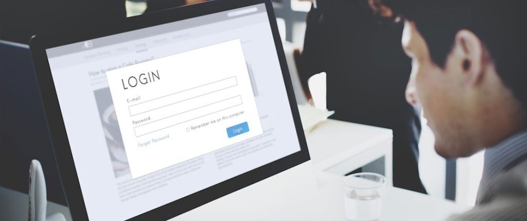 A man sits at a desk looking at a computer screen displaying a login page with fields for email and password. The office background is blurred, emphasizing the concept of secure access or user authentication.