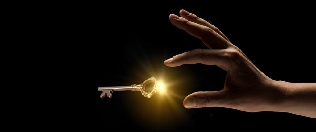 A hand reaches toward a glowing golden key against a dark background. The light from the key creates a warm glow, symbolizing opportunity, success, or discovery.
