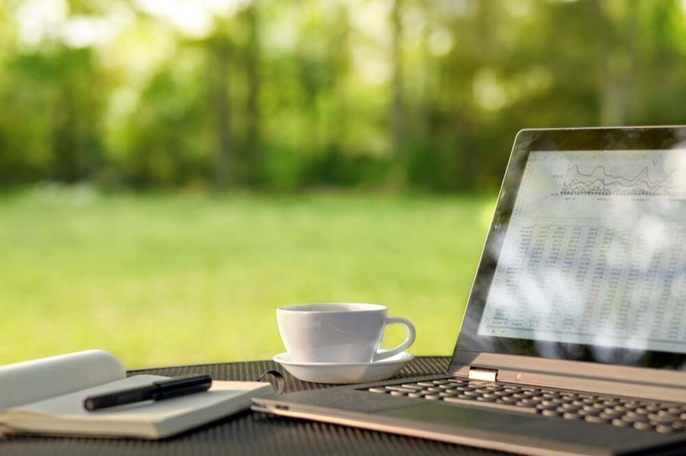 A laptop displaying data charts sits on an outdoor table beside a cup of coffee, notebook, and pen, symbolizing remote work or digital productivity in a natural setting.