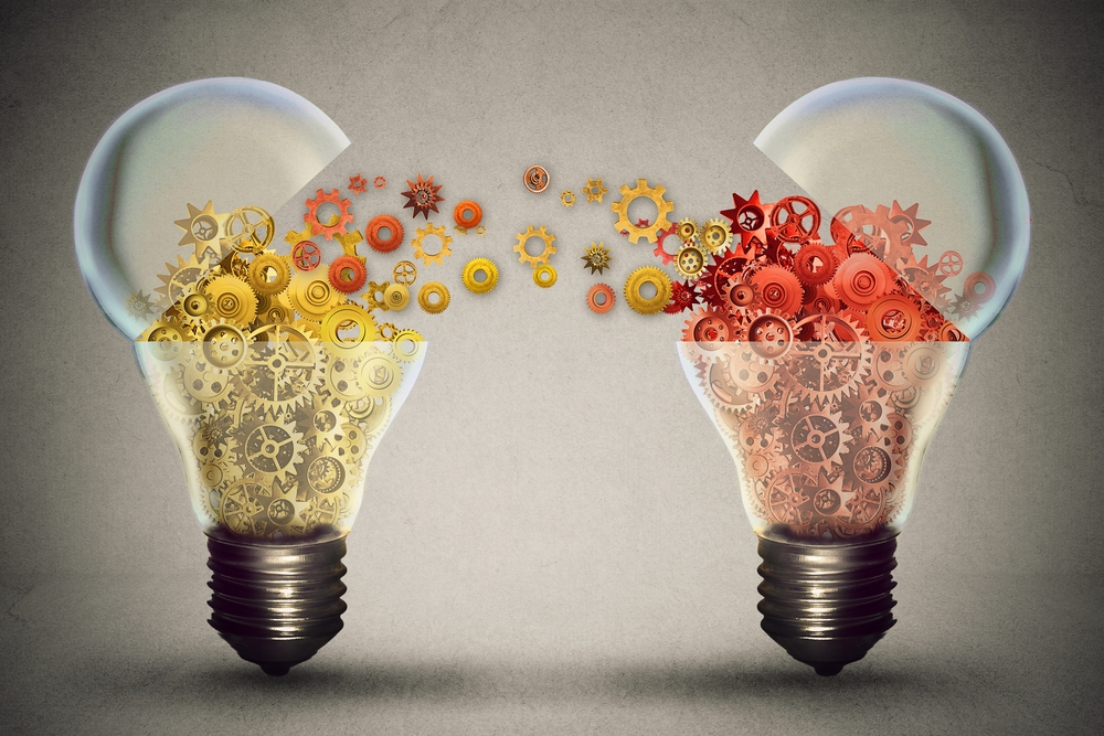Conceptual image showing two light bulbs filled with colorful gears, with yellow gears flowing from the left bulb to the right red one, symbolizing idea sharing, creativity, or knowledge transfer.