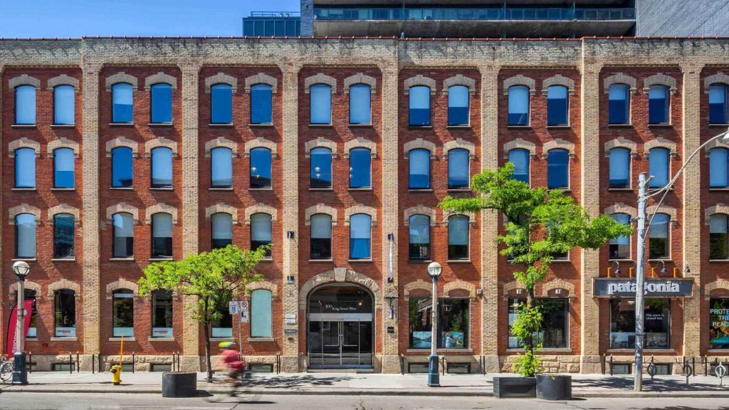 Historic red-brick building with arched windows and retail shops at street level, including a Patagonia store, on a sunny urban street.