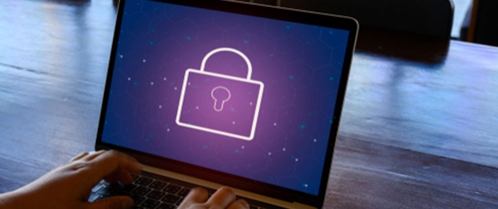 Person typing on a laptop displaying a large glowing padlock icon on the screen – dark background with digital network patterns; symbolizes cybersecurity, data protection, or secure system access.