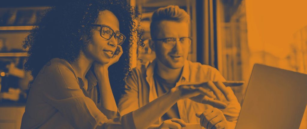A man and a woman sit together at a table, looking at a laptop screen while discussing something. The image has an orange color overlay, giving it a modern and creative tone that suggests teamwork and collaboration.