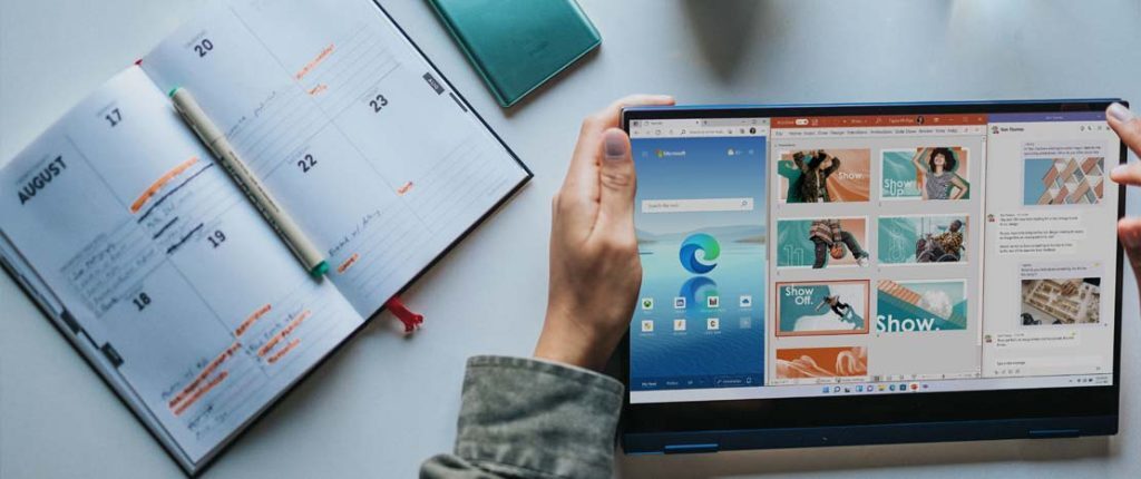 A person holds a laptop displaying a split screen with a web browser and a presentation design tool open. The workspace also includes an open planner with dates marked in August, suggesting planning and digital content creation.