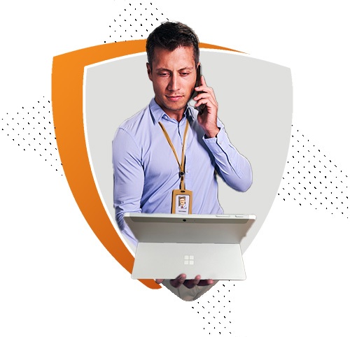 A man wearing a light blue shirt and an ID badge is talking on the phone while looking at a laptop. The image is set within an orange and white shield shape, representing professionalism and secure communication.