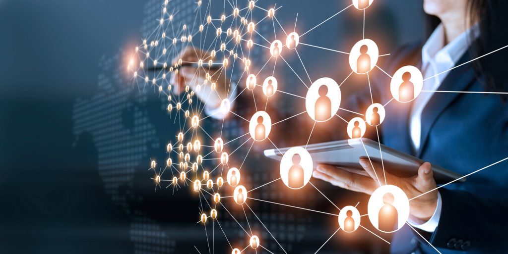 Conceptual image of digital networking showing a business professional holding a tablet and interacting with a glowing web of interconnected user icons. The background includes a faint world map, symbolizing global communication, data sharing, and online collaboration.