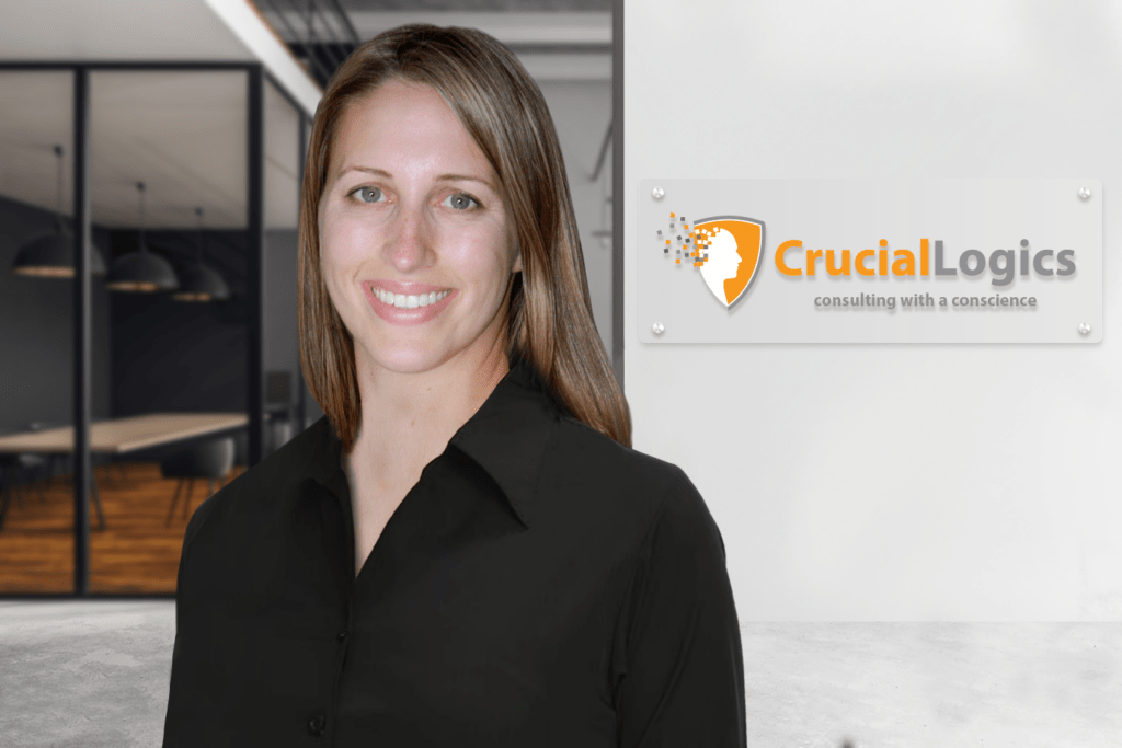 A woman wearing a black collared shirt stands smiling in a modern office setting; the Crucial Logics logo with the tagline consulting with a conscience is visible on the wall behind her.