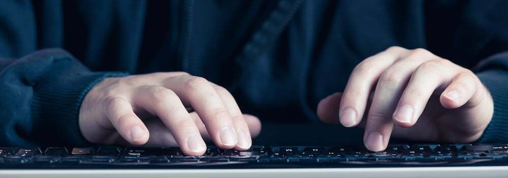 A close-up of hands typing on a keyboard in a dimly lit setting; suggesting hacking, programming, or cybersecurity activity.